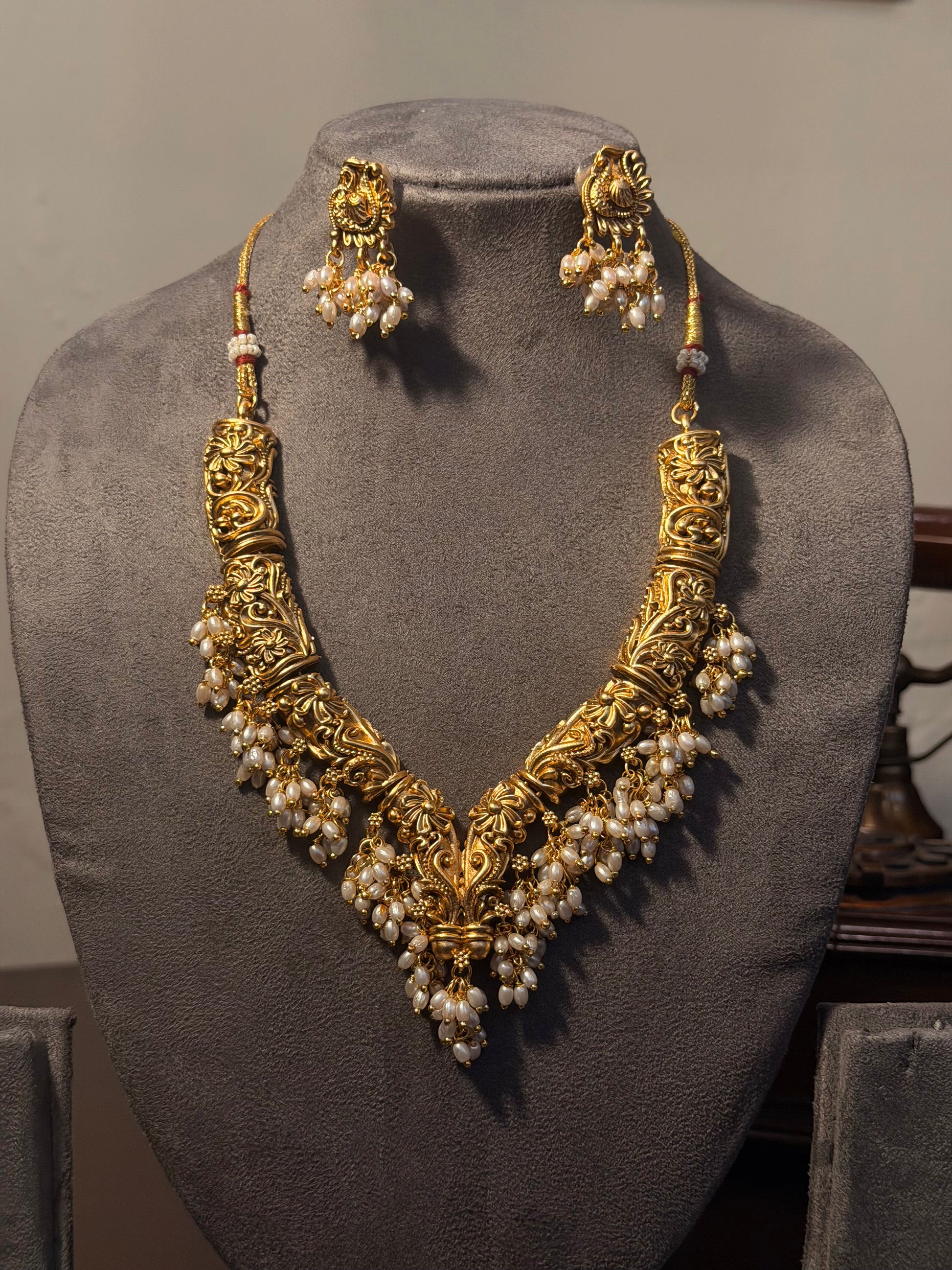 Gold necklace with pearl drops and matching earrings on a gray mannequin bust.